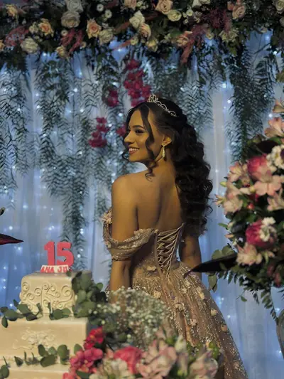 Debutante de vestido dourado diante do bolo de 15 anos