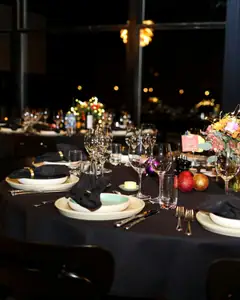 Mesa redonda posta com toalha escura e flores em salão de festa